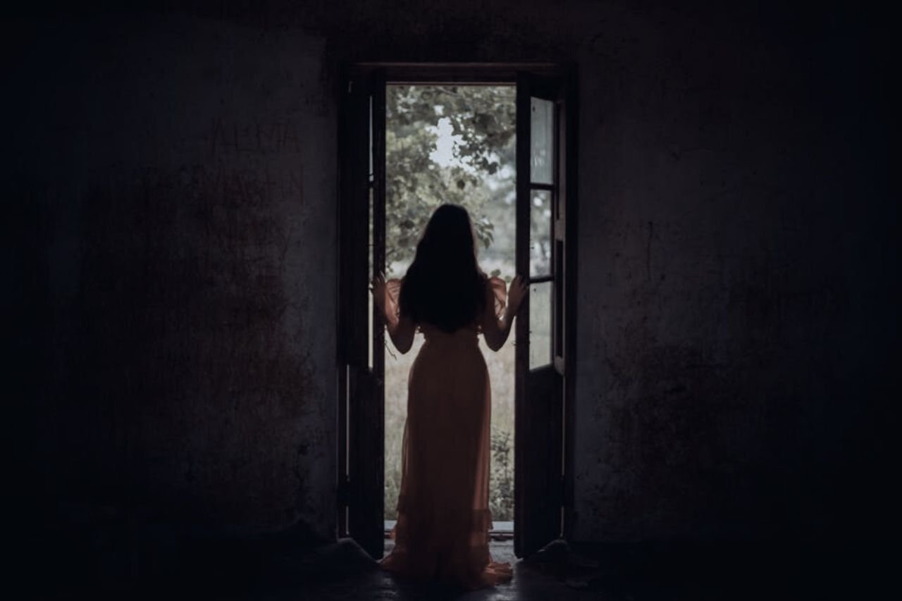 Woman standing in a doorway between darkness and light, symbolizing the difference between wanting and needing in relationships